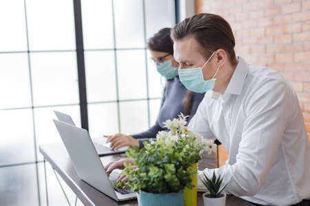 businessman and businesswoman wear a face mask for protecting the virus while working in a coffee...