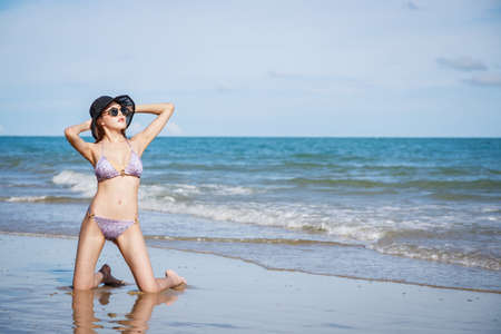 Outdoor summer portrait of Asian beautiful girl in a sexy bikini sitting on the beach in summer. teenage girls. sexy body. concept vacation, holiday in summer and blue skyの写真素材