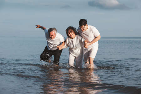 Asian senior couple and son walking on summer beach sunset. Travel leisure and activity after...