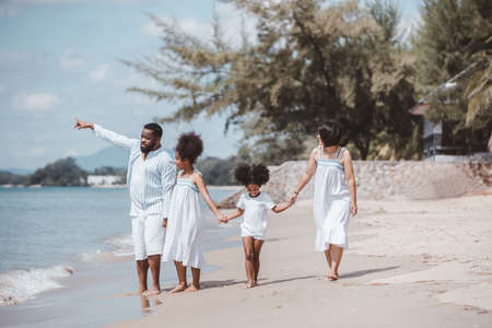 African American family. Happy family (Mother, Father, Two daughters) walking and playing together on the beach on holiday, having fun on a tropical beach. Summer vacation family.の写真素材