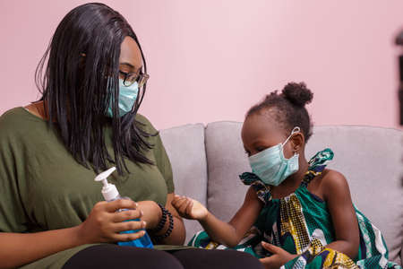African Americans' mother and daughter wearing a mask are washing their hands with alcohol to protect them from germs and COVIC 19 while staying at home. black people or African Americansの写真素材