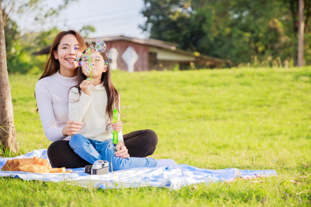 Happy family picnic. A little girl blowing soap bubbles with parents (Father, Mother) with fun and enjoyed together during picnicking on picnic cloth. family relaxes in green park. Family weekendの写真素材