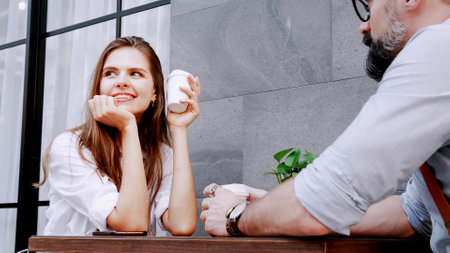 Happy caucasian man and woman enjoying coffee and smiling while sitting on cafe terrace. Portrait of woman and man relaxing in outdoors cafe and drinking coffee during romantic date.の写真素材