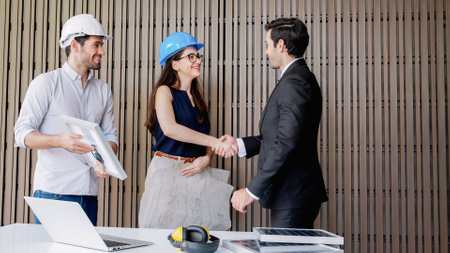 Two engineers working and shaking hands with partnership deal executive meeting in the office. They are discussing project plan solar panels power teamwork and then celebrating success together.の写真素材