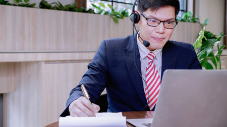 Businessman wearing telephone headset talking to caller in customer services department. Male...