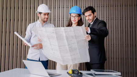 Two engineers working with blueprints sketching a project with partner in the office. They are discussing project plan solar panels power teamwork and then celebrating success together. Design concept.の写真素材
