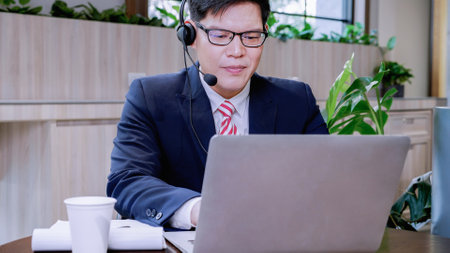 Businessman wearing telephone headset talking to caller in customer services department. Male professional call center agent, having distance webcam chat job interview on computer at home office.の写真素材