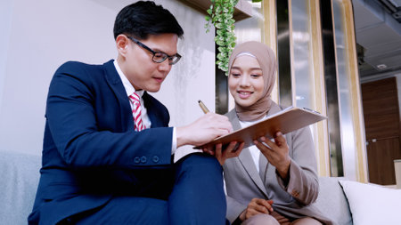 Two male and female hijab business colleagues using digital tablet, notepad and discussing project...