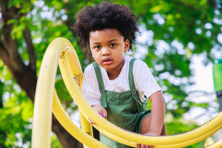 Cute African American little kid boy having fun while playing on the playground in the daytime in...