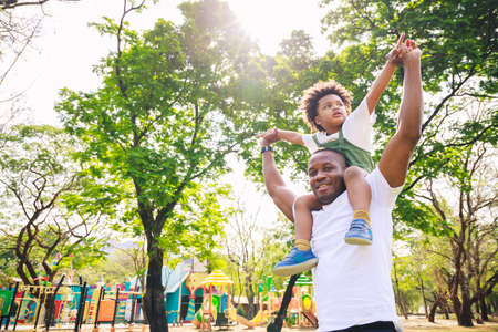 African American father giving son ride on back at park. family playing togetherness and relaxes. Family weekend. Cute African American boy with dad playing outdoor.の写真素材