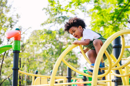 Cute African American little kid boy having fun while playing on the playground in the daytime in summer. Outdoor activity. Playing make believe concept. Outside educationの写真素材