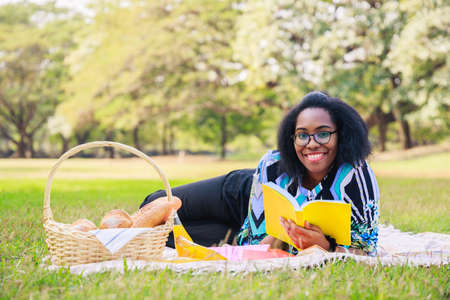 Happy young African American woman reading an interesting book. A cheerful African American woman in the park in the summertime. Young African American studentの写真素材