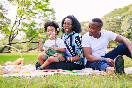 Happy African American family life concept. African American parents (Father, Mother) and little boy enjoying during playing soap bubbles togetherness. family relaxes in green park. Family weekend.の写真素材