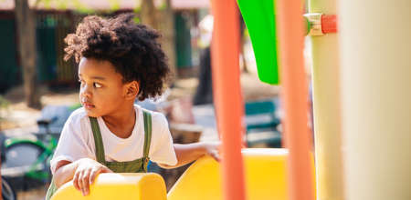 Cute African American little kid boy having fun while playing on the playground in the daytime in summer. Outdoor activity. Playing make believe concept. Outside educationの写真素材