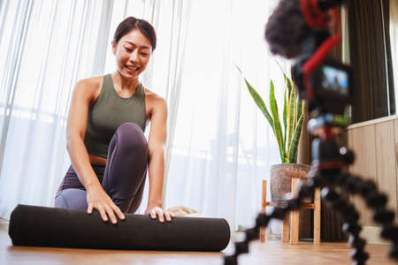 Asian woman yoga teacher filming yoga online class on video for Social media. Professional instructor in sportswear posing on VIDEO camera. Healthy lifestyle - technology at home. New normal lifestyleの写真素材