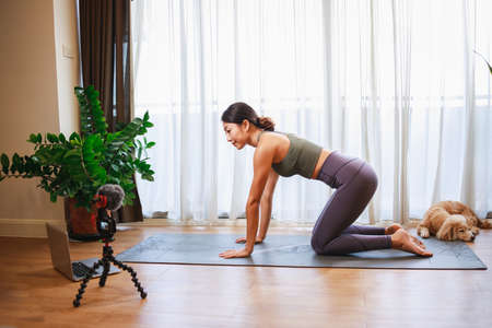 Asian woman yoga teacher filming yoga online class on video for Social media. Professional instructor in sportswear posing on VIDEO camera. Healthy lifestyle - technology at home. New normal lifestyleの写真素材