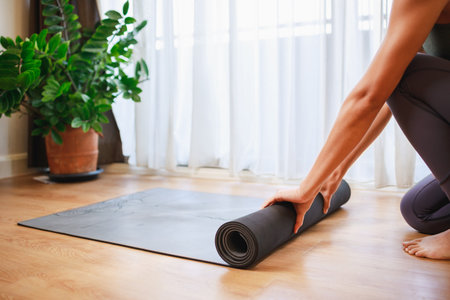 Close-up of woman hands unrolling roll black yoga mat for playing yoga at home for quarantine herself from Covid-19, New normal lifestyle conceptの写真素材