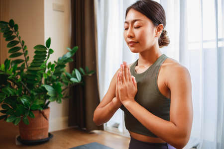 Asian woman in sports clothing doing yoga at home to quarantine herself from Covid-19, New normal lifestyle concept. Healthy lifestyle. Relaxing at homeの写真素材