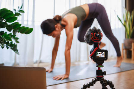 Asian woman yoga teacher filming yoga online class on video for Social media. Professional instructor in sportswear posing on VIDEO camera. Healthy lifestyle - technology at home. New normal lifestyleの写真素材
