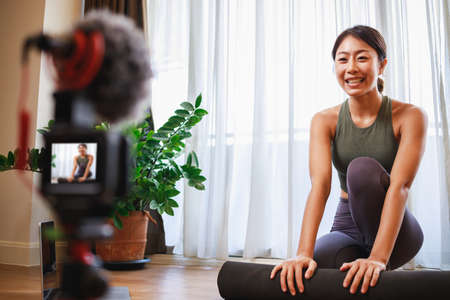 Asian woman yoga teacher filming yoga online class on video for Social media. Professional instructor in sportswear posing on VIDEO camera. Healthy lifestyle - technology at home. New normal lifestyleの写真素材