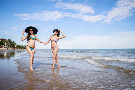 Outdoor summer portrait of the front image of two Asian beautiful girls in a sexy bikini standing on the beach in summer. teenage girls best friends. sexy body. concept vacation, holiday in summerの写真素材