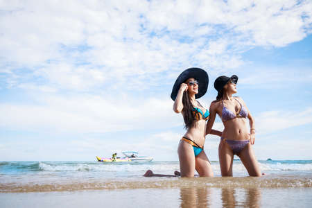 Outdoor summer portrait of the front image of two Asian beautiful girls in a sexy bikini sitting on the beach in summer. teenage girls best friends. sexy body. concept vacation, holiday in summerの写真素材