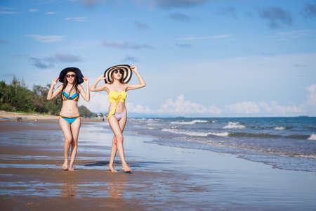 Outdoor summer portrait of the front image of two Asian beautiful girls in a sexy bikini standing on the beach in summer. teenage girls best friends. sexy body. concept vacation, holiday in summerの写真素材