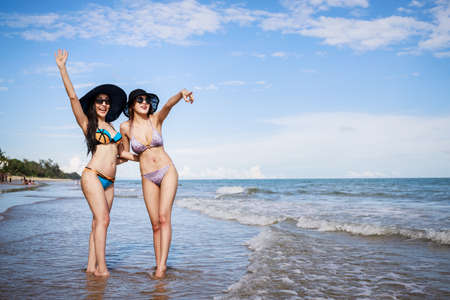 Outdoor summer portrait of the front image of two Asian beautiful girls in a sexy bikini standing on the beach in summer. teenage girls best friends. sexy body. concept vacation, holiday in summerの写真素材