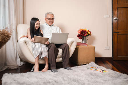 Happy Asian retirement grandfather and pretty granddaughter watching e-book for learning to education together by laptop. Happy Family educational at home concept. Technology and education.の写真素材