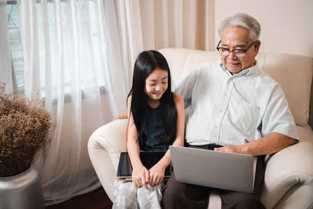 Happy Asian retirement grandfather and pretty granddaughter watching e-book for learning to education together by laptop. Happy Family educational at home concept. Technology and education.の写真素材