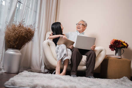 Happy Asian retirement grandfather and pretty granddaughter laughing while watching e-book for learning to education together by laptop. Family educational at home concept. Technology and education.の写真素材
