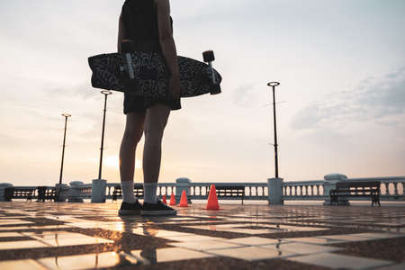 Asian woman leg holding surf skate or skate board in outdoor Park at sunset. sport training for trendy people.の写真素材