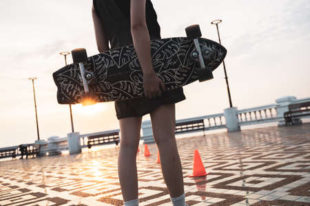 Asian woman leg holding surf skate or skate board in outdoor Park at sunset. sport training for trendy people.の写真素材