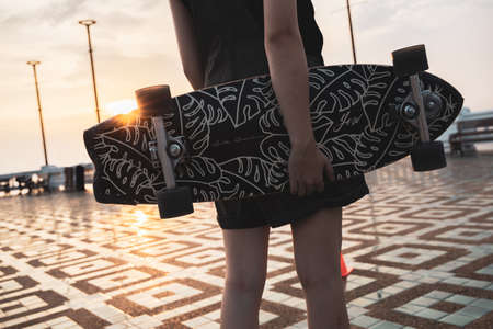 Asian woman leg holding surf skate or skate board in outdoor Park at sunset. sport training for trendy people.の写真素材