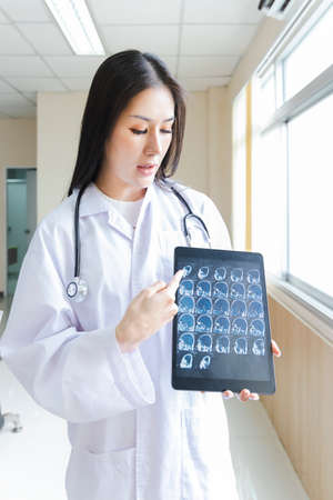 portrait of smart female doctor holding tablet to show X-Ray picture and standing at reception of the hospital.の写真素材