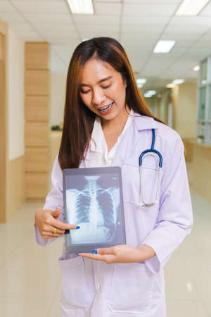 portrait of smart female doctor holding tablet to show X-Ray picture and standing at reception of...