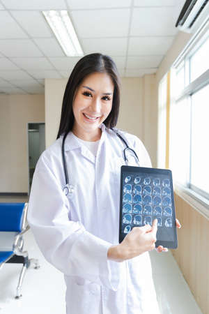 portrait of smart female doctor holding tablet to show X-Ray picture and standing at reception of the hospital.の写真素材
