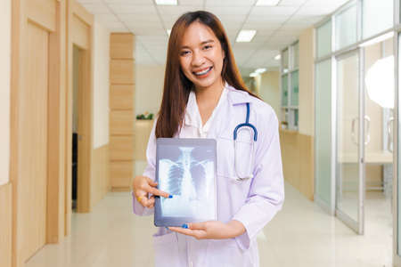 portrait of smart female doctor holding tablet to show X-Ray picture and standing at reception of the hospital.の写真素材