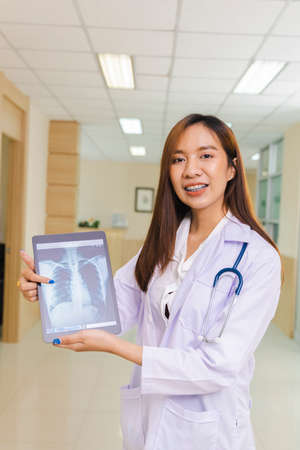 portrait of smart female doctor holding tablet to show X-Ray picture and standing at reception of the hospital.の写真素材