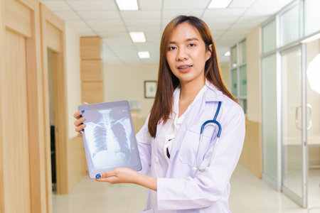 portrait of smart female doctor holding tablet to show X-Ray picture and standing at reception of the hospital.の写真素材