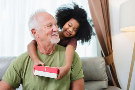 African American girl surprise her  senior grandfather for Christmas gift at homeの写真素材