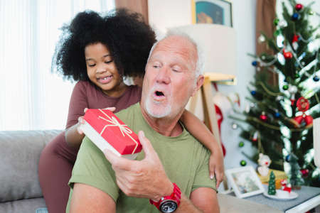 African American girl surprise her  senior grandfather for Christmas gift at homeの写真素材