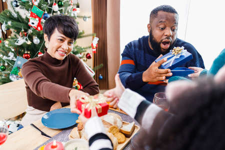 African American family surprising together with a gift on Christmas day while dinner. Merry Christmas. Happy family.の写真素材
