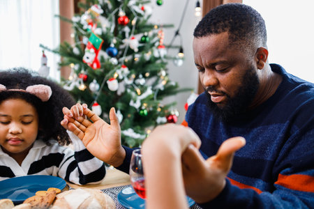Families together to pray before meals at home. Celebration holiday togetherness near Christmas tree. African American family. Merry Christmas.の写真素材