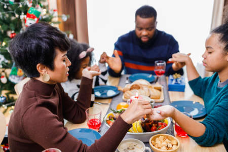 Families together to pray before meals at home. Celebration holiday togetherness near Christmas tree. African American family. Merry Christmas.の写真素材