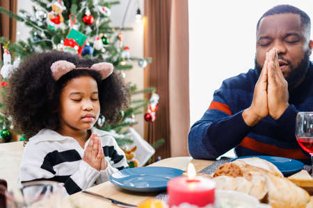 Families together to pray before meals at home. Celebration holiday togetherness near Christmas tree. African American family. Merry Christmas.の写真素材