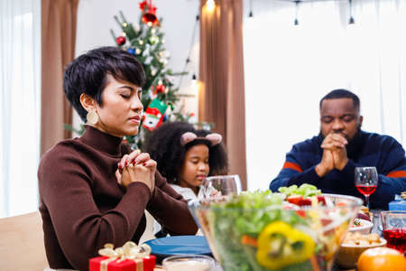 Families together to pray before meals at home. Celebration holiday togetherness near Christmas tree. African American family. Merry Christmas.の写真素材