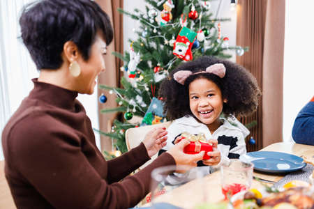 African American family surprising together with a gift on Christmas day while dinner. Merry Christmas. Happy family.の写真素材