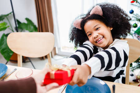 African American family surprising together with a gift on Christmas day while dinner. Merry Christmas. Happy family.の写真素材