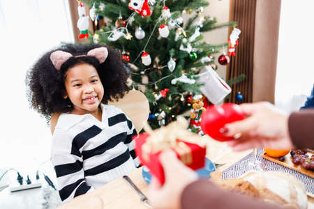 African American family surprising together with a gift on Christmas day while dinner. Merry Christmas. Happy family.の写真素材